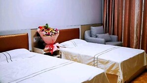 Une chambre d’hôtel avec deux lits, un canapé gris, un bouquet de fleurs et un rideau.
