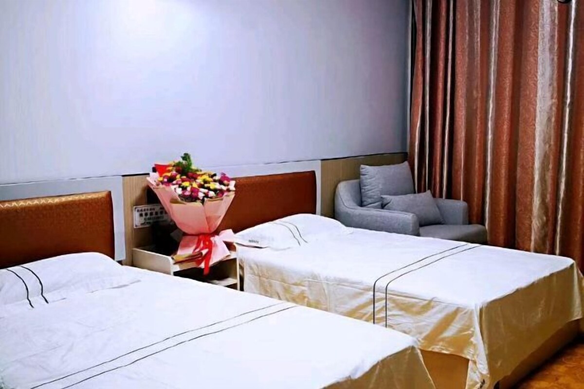 Habitación de hotel con dos camas, un sofá gris, un ramo de flores y una cortina.