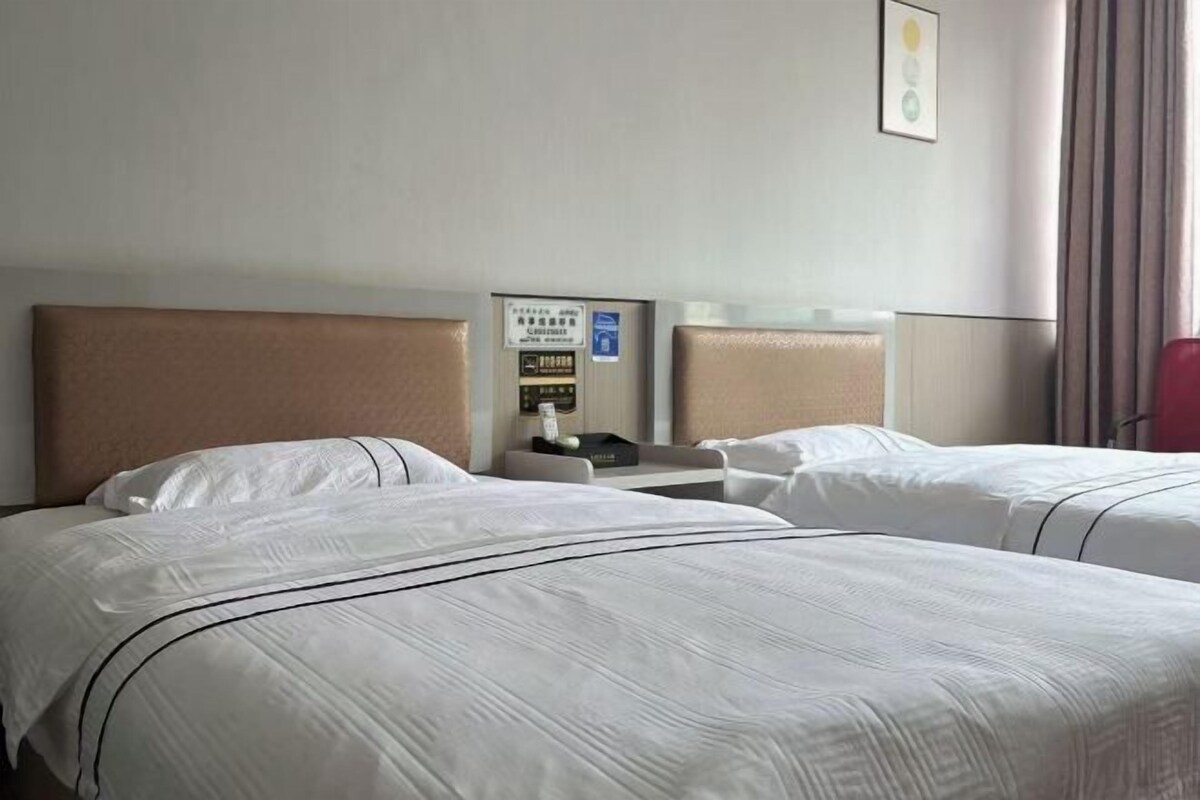 Une chambre d’hôtel avec deux lits, une table de chevet, un panneau de commande fixé au mur et une fenêtre avec des rideaux.