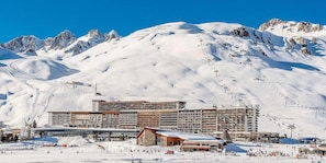 Un hotel de varios pisos, con pistas de esquí al fondo y un paisaje montañoso.