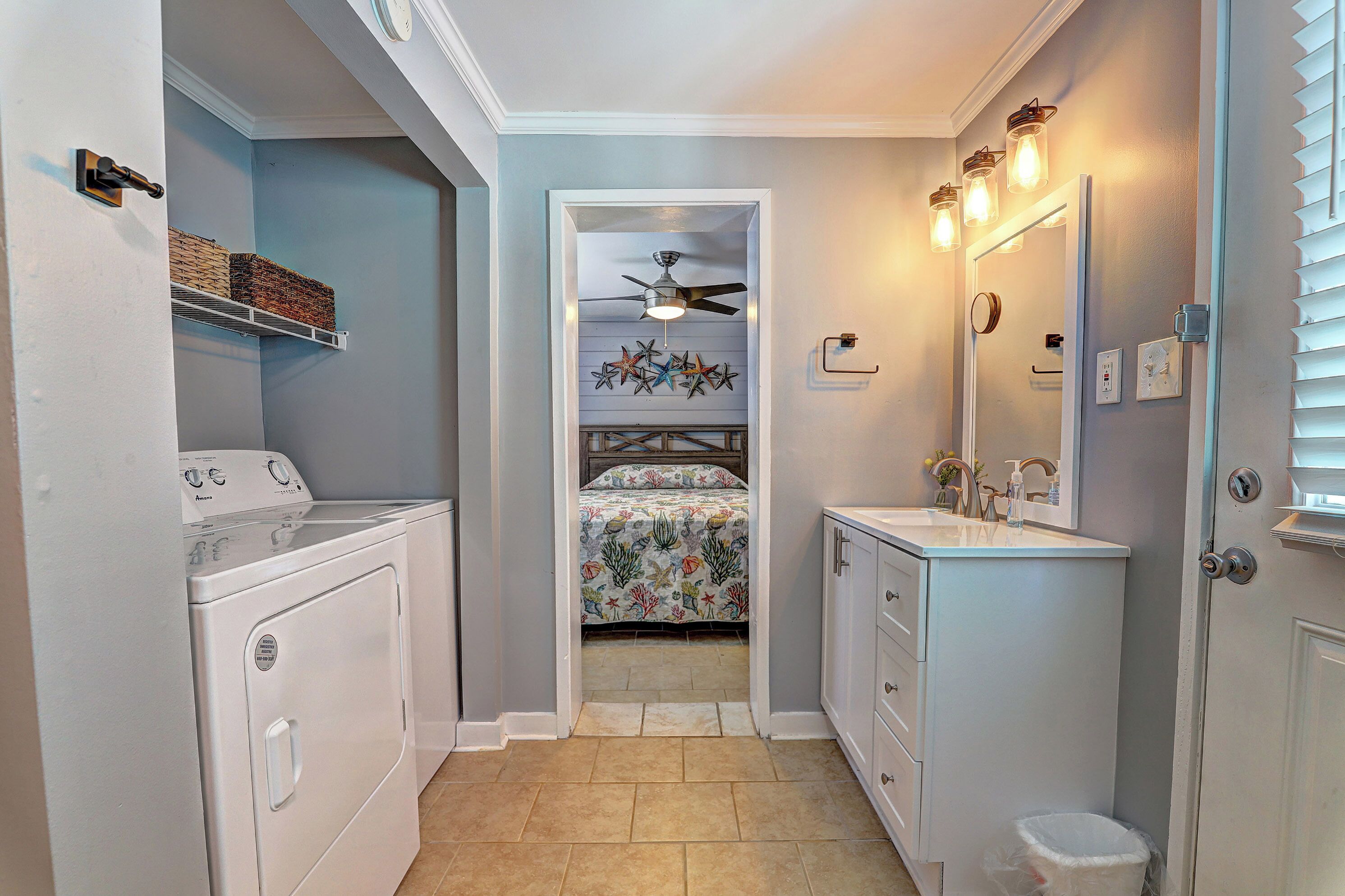 Une petite salle de bain équipée d’un lave-linge, d’un lit avec une couvre-lit à motifs floraux, d’un ventilateur de plafond et d’un lavabo avec un miroir.