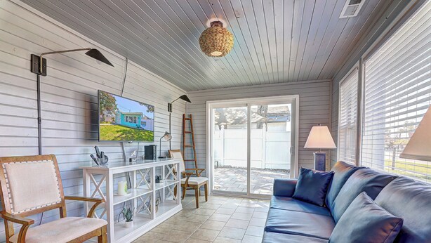 A living room with a blue leather sofa, a wooden chair, a TV on the wall, and a white console table. - Cottage on the Rocks - 3 Bedrooms - Walk to Beach - Outdoor Seating - Pet Friendly (North Myrtle Beach)