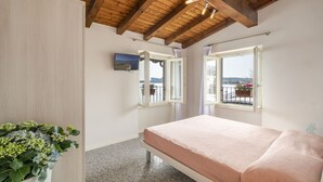 A bedroom with a wooden ceiling, a bed, a potted plant, and a view of a balcony with flowers. - Apartment in Manerba with barbecue (Manerba sul Garda)
