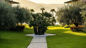 A pathway leading to a building surrounded by lush greenery and palm trees, with mountains in the background. - Apartment in Manerba with barbecue (Manerba sul Garda)