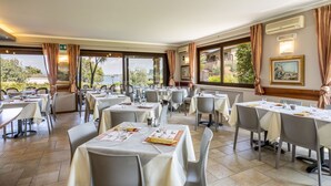 A restaurant with tables set for dining, large windows with curtains, and a view of the outdoors. - Apartment in Manerba with barbecue (Manerba sul Garda)