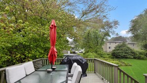 Eine Terrasse im Freien mit einem Tisch und Stühlen mit Glasplatte, einem roten Sonnenschirm und einem schwarzen Sonnenschirm.