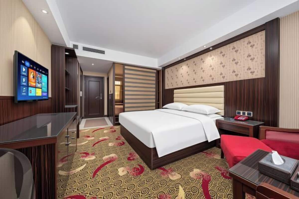 A hotel room with a bed, a TV, a desk, and a red chair.