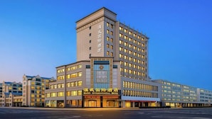 Un hotel de varios pisos con una torre angular destacada, múltiples balcones y una entrada amplia con señalización.