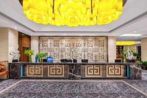 Un'area della reception di un hotel con un bancone in marmo, una parete decorata con motivi geometrici e un lampadario moderno.
