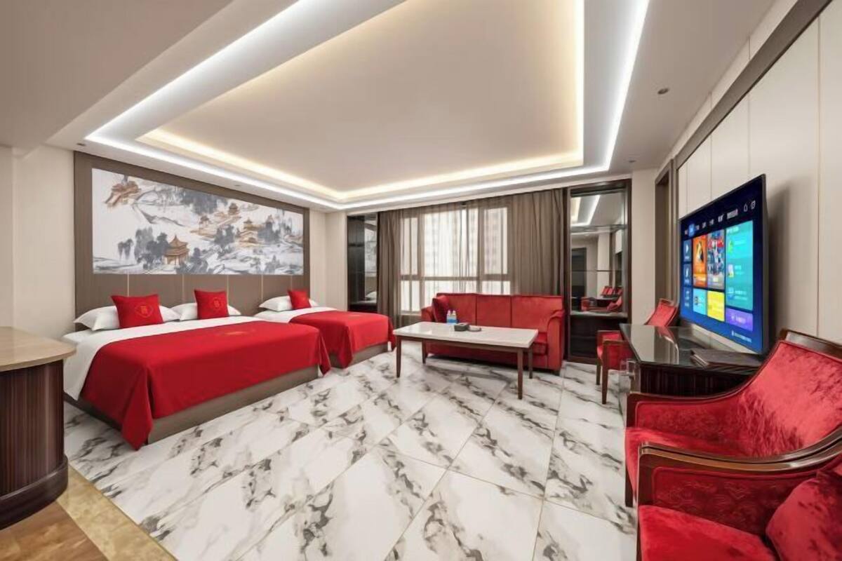 A hotel room with a bed, two red sofas, a TV, and a marble floor.