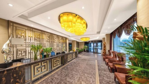 Vestíbulo de hotel con mostrador de recepción, zona de estar, paneles decorativos y una araña.