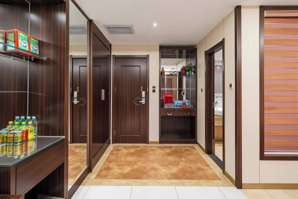 A hallway with a wooden wardrobe, a glass shelf with bottles, and a mirror.