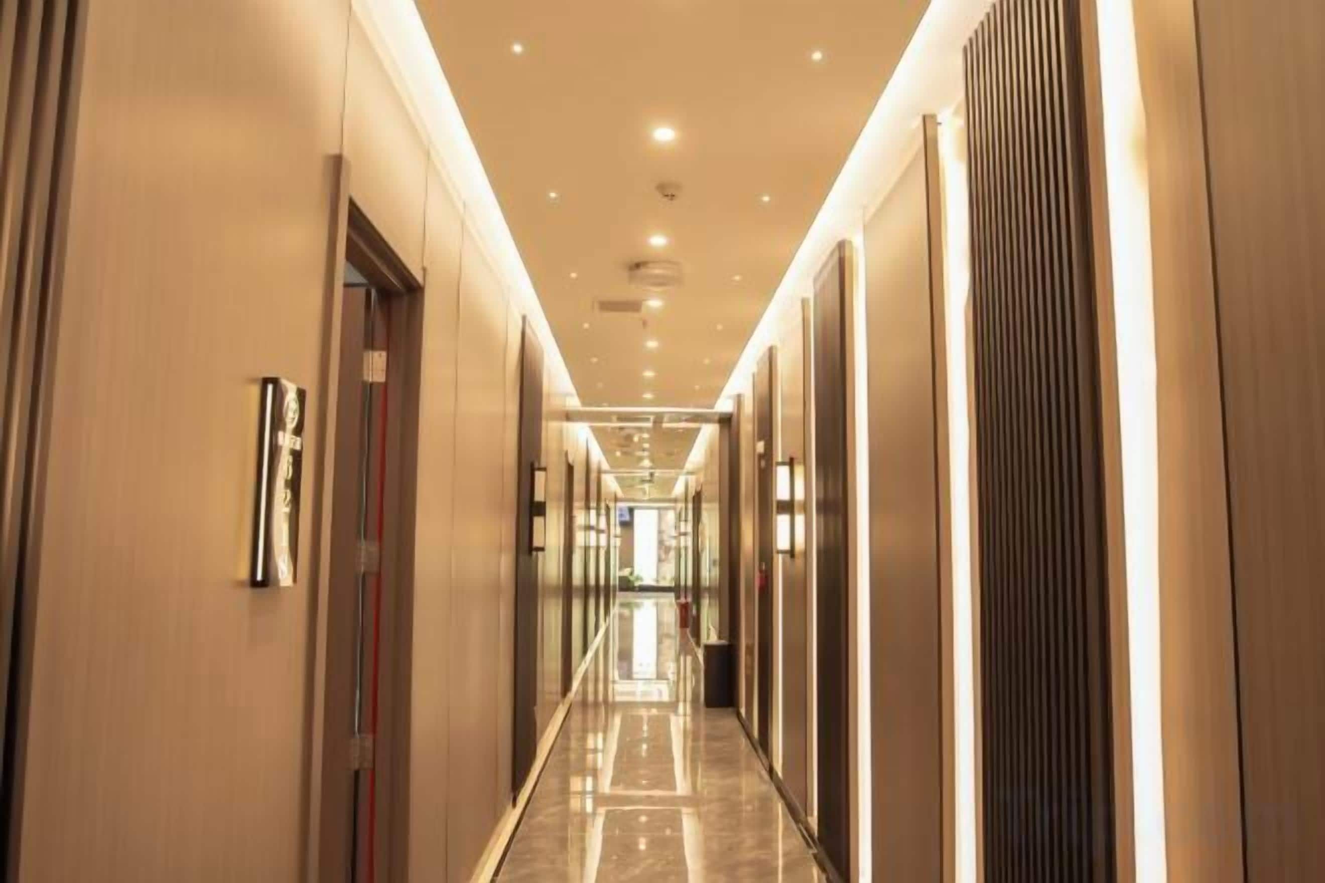 Passadís llarg i estret d'un hotel, amb portes a banda i banda, il·luminació empotrada i un sòl polit.