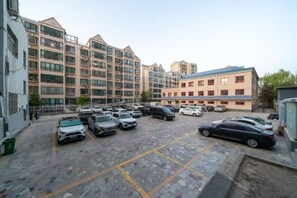 A parking lot with multiple cars, a building with a blue roof, and a multi-story residential building in the background. - Hanwu International Hotel (Wuwei Pedestrian Street Branch) (Wuwei)