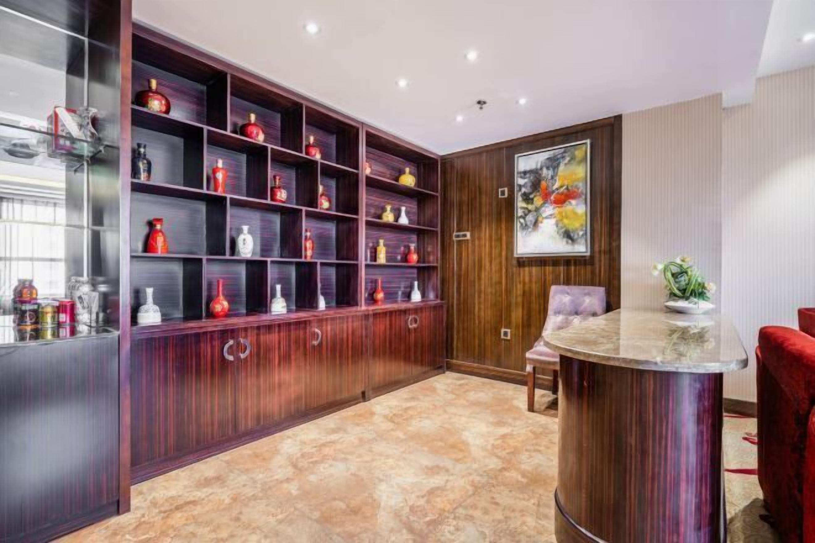 Un interior moderno con un mueble de madera lleno de botellas, una encimera de mármol y un cuadro abstracto enmarcado.