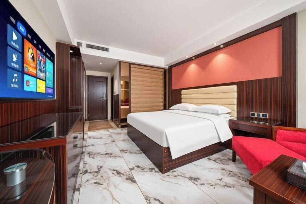 A modern hotel room with a large bed, a TV, a wooden wardrobe, and a red chair.