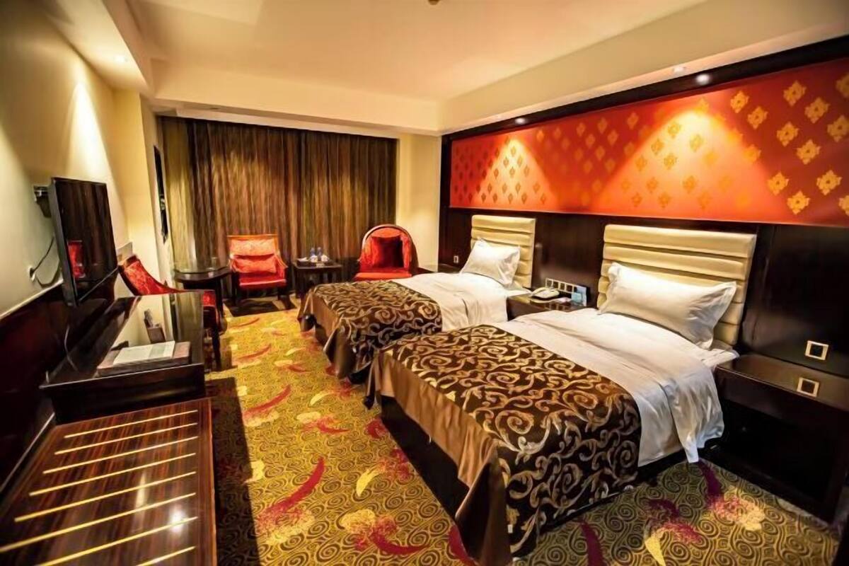 A hotel room with two beds, a desk, a chair, and a television.