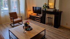 En stue med fjernsyn, pejs, en lænestol og et sofabord med blomster.