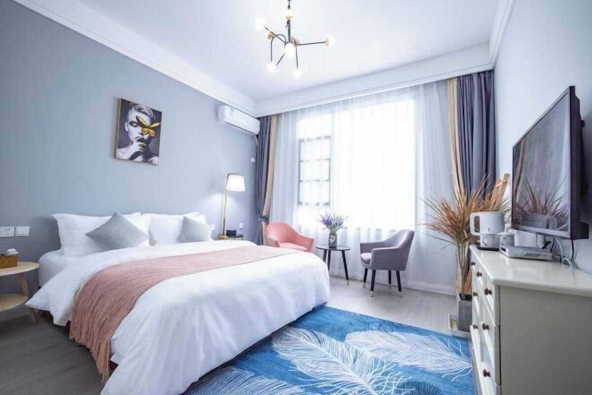 Moderni hotellihuone, jossa on suuri sänky, työpöytä, tuoli, televisio ja ikkuna, jossa on verhot.