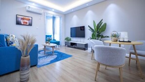 A modern living room with a blue sofa, a coffee table, a TV, and a dining area with a table and chairs. - Hongye Inn (Dujiangyan)