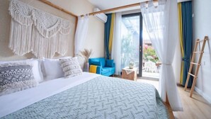 A bedroom with a bed, a blue chair, a small table, and a balcony with curtains. - Hongye Inn (Dujiangyan)