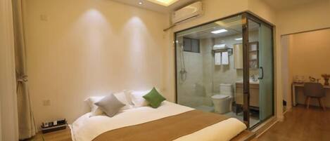A modern bedroom with a large bed, a glass shower enclosure, and a small desk area.