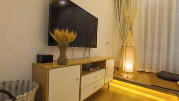 A modern living room with a flat-screen TV mounted on the wall, a wooden cabinet with drawers, a wicker basket, and a floor lamp.