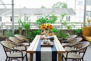 An outdoor dining area with a table set for four, surrounded by wicker chairs, and a view of traditional buildings in the background. - Hongye Inn (Dujiangyan)