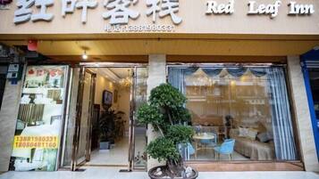 A hotel entrance with a sign reading "Red Leaf Inn" and a contact number. There is a potted plant in the foreground.