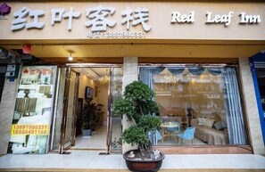 A hotel entrance with a sign reading "Red Leaf Inn" and a contact number. There is a potted plant in the foreground. - Hongye Inn (Dujiangyan)