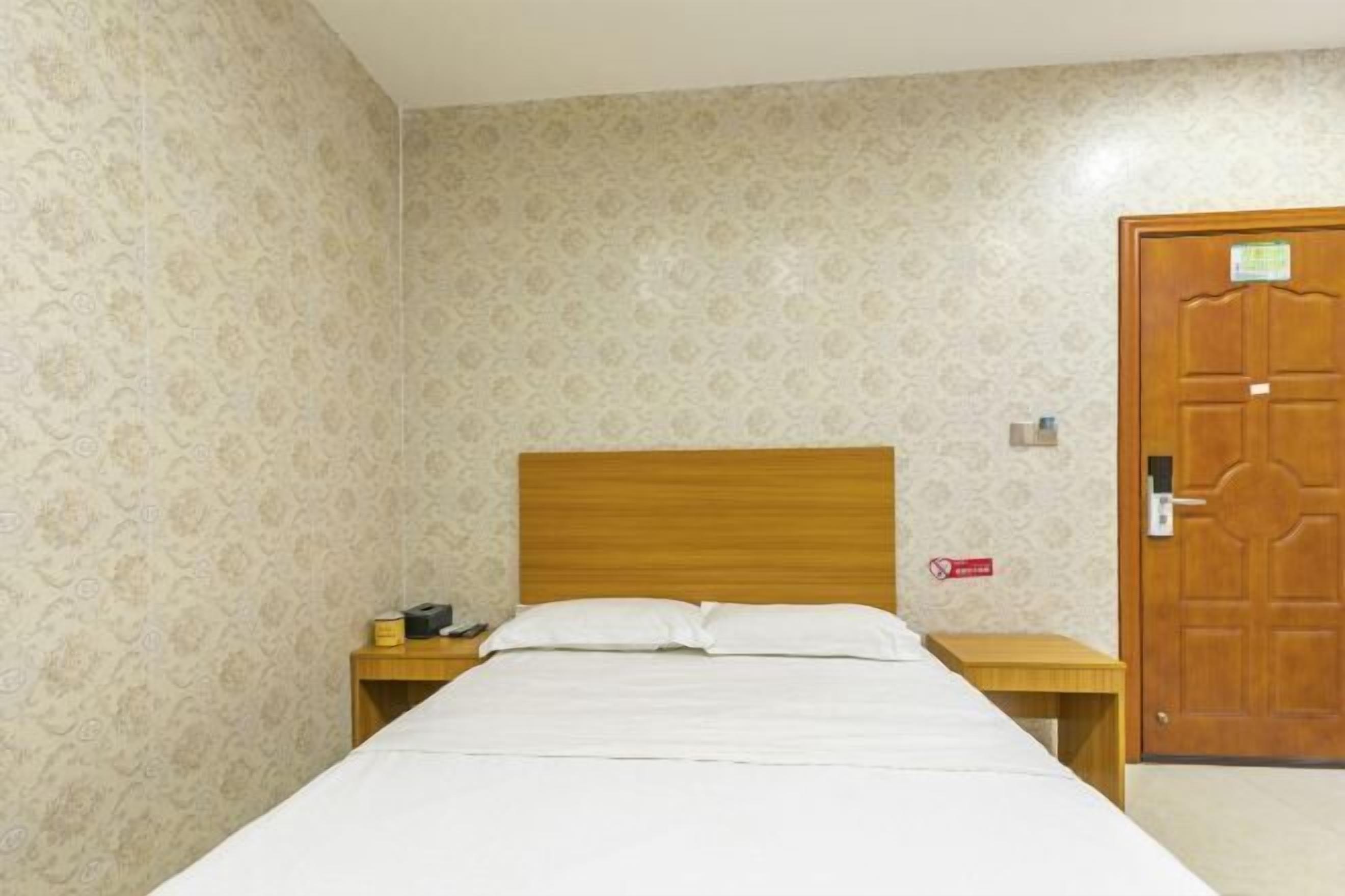A room with a bed, a wooden headboard, a nightstand with a lamp, and a door with a lock.