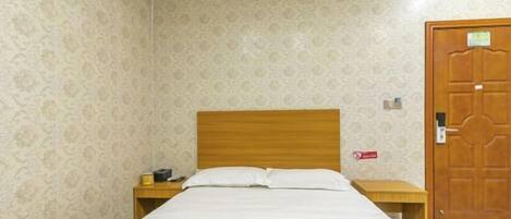 A room with a bed, a wooden headboard, a nightstand with a lamp, and a door with a lock.