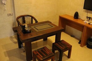 A small, compact room with a wooden table, two matching stools, a chair, a small cabinet, and a television mounted on the wall. - Jiangdao Hostel (Jiangmen)