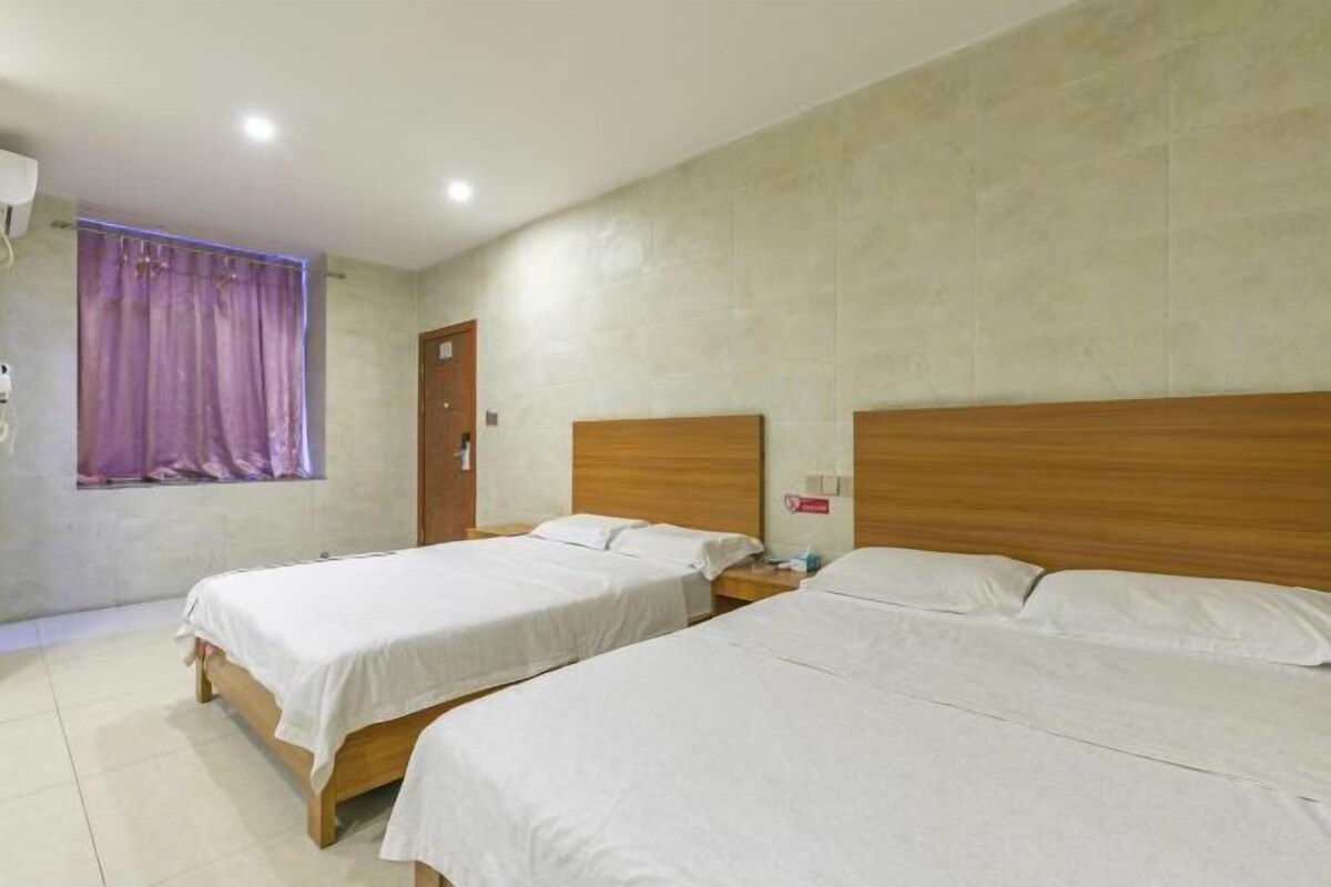A hotel room with two beds, a window with purple curtains, and a wooden headboard.
