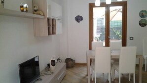 Ein moderner Wohnraum mit Flachbildfernseher, einem Essbereich mit weißen Stühlen und einer Holzkabine mit Dekorationselementen.