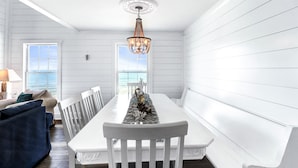 A dining area with a white table and bench, a chandelier, and a view of the ocean through large windows. - 4 Bed/3 Bath North Cape San Blas Beach Front Home - Steps to the Water!! (Port St. Joe)
