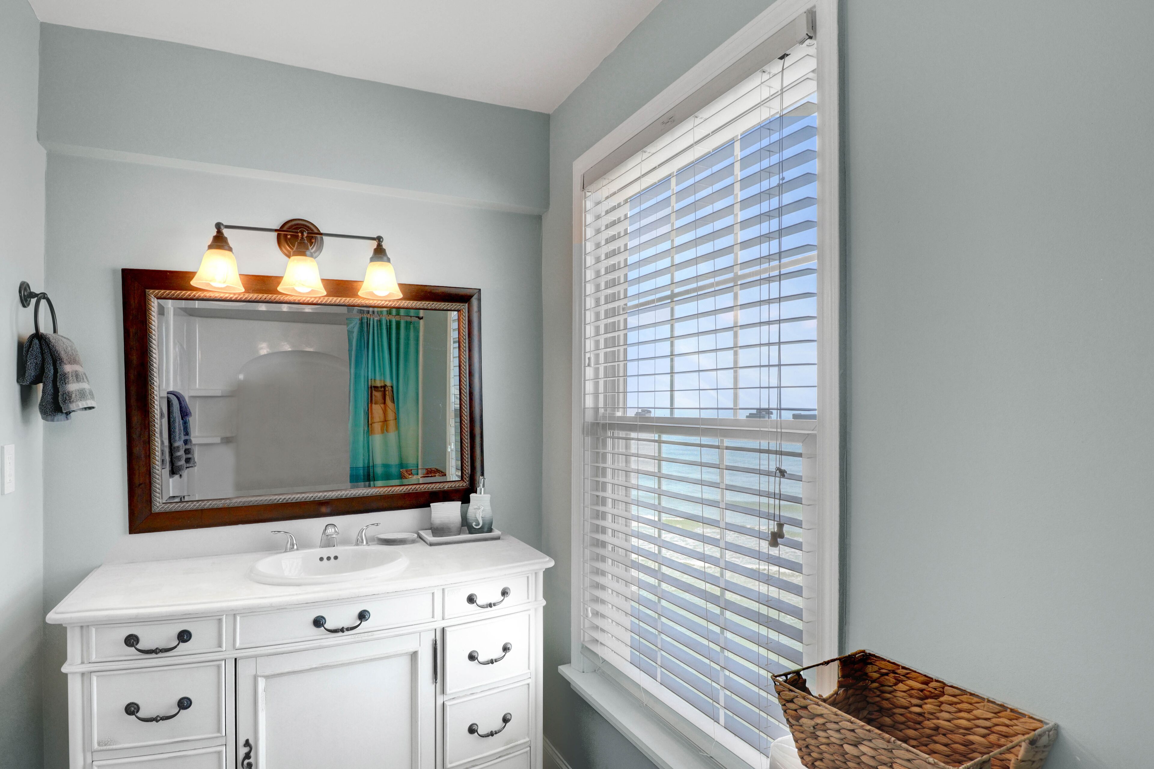 A bathroom with a white vanity, a large mirror, and a window with blinds.