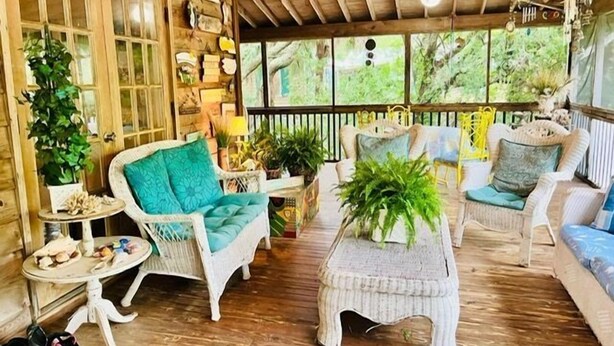 L’intérieur d’un chalet en bois rustique et chaleureux, avec des meubles en osier, un plancher en bois et une grande fenêtre donnant sur un paysage verdoyant.