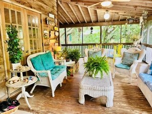 Interior acolhedor de uma cabana rústica de madeira, com móveis de vime, piso de madeira e uma grande janela com vista para o verde lá fora.
