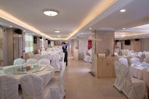Un salón de banquetes con mesas redondas cubiertas con manteles blancos y sillas, una estación central de servicio y un largo pasillo.