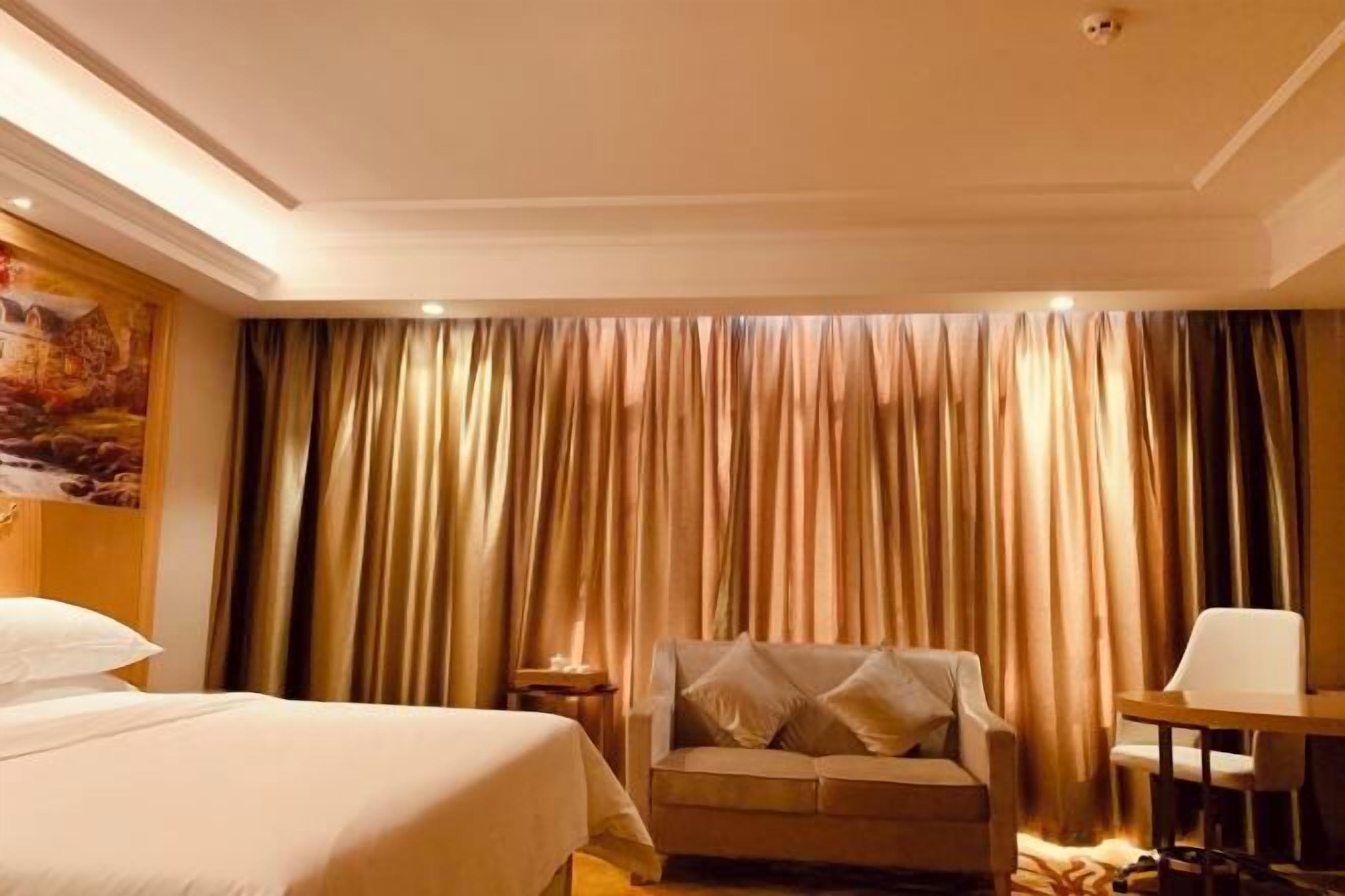 A hotel room with a bed, a sofa, a table, and curtains.