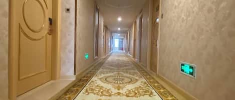 A long, narrow hallway with ornate patterned carpet and beige walls.