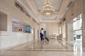 A spacious lobby with a marble reception desk, a chandelier, and a person with luggage. - Vienna Hotel (Jieyang Longwei) (Jieyang)