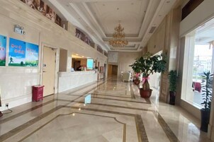 Un vestíbulo de hotel con mostrador de recepción, una araña y plantas en macetas.