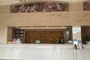A hotel reception area with a marble counter, a receptionist, and a mural above.