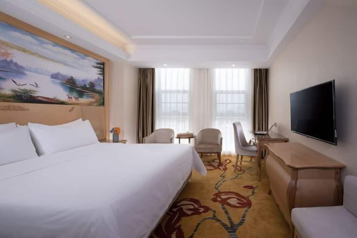 Quarto de hotel com cama, escrivaninha, televisão e um quadro na parede.
