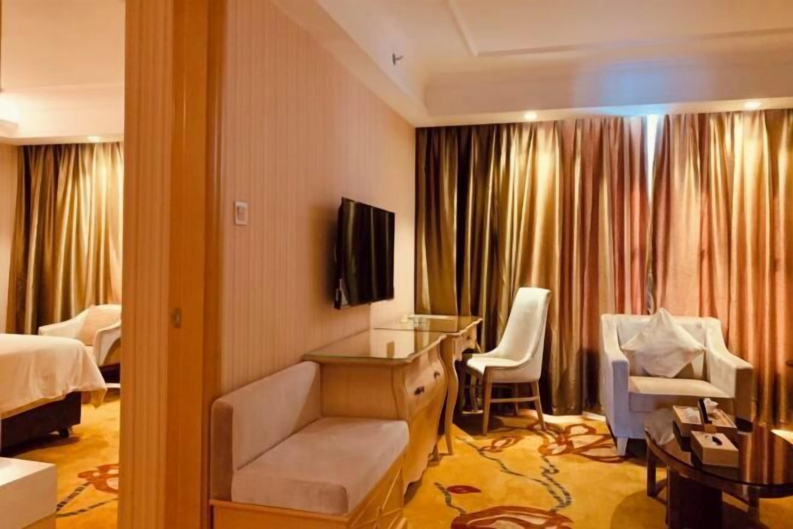 A hotel room with a bed, a desk with a chair, a television, and a sofa.