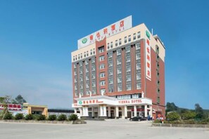A multi-story hotel with a prominent sign at the top, a large entrance with a covered area, and a parking lot in front.
