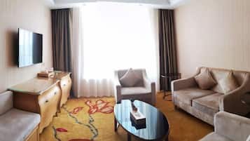 A hotel room with a flat-screen TV, a sofa, a chair, a coffee table, a desk, and a large window with curtains.