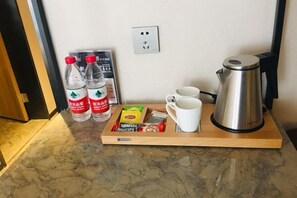 Bandeja de desayuno con agua embotellada, una cafetera y una caja de café instantáneo sobre una encimera de mármol.